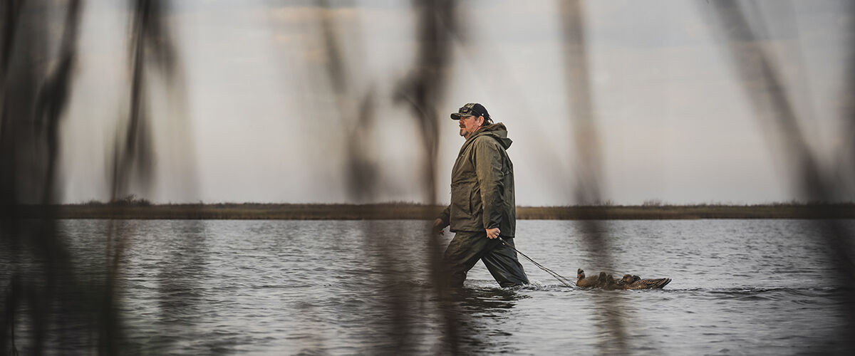 man walking through water with duck decoys